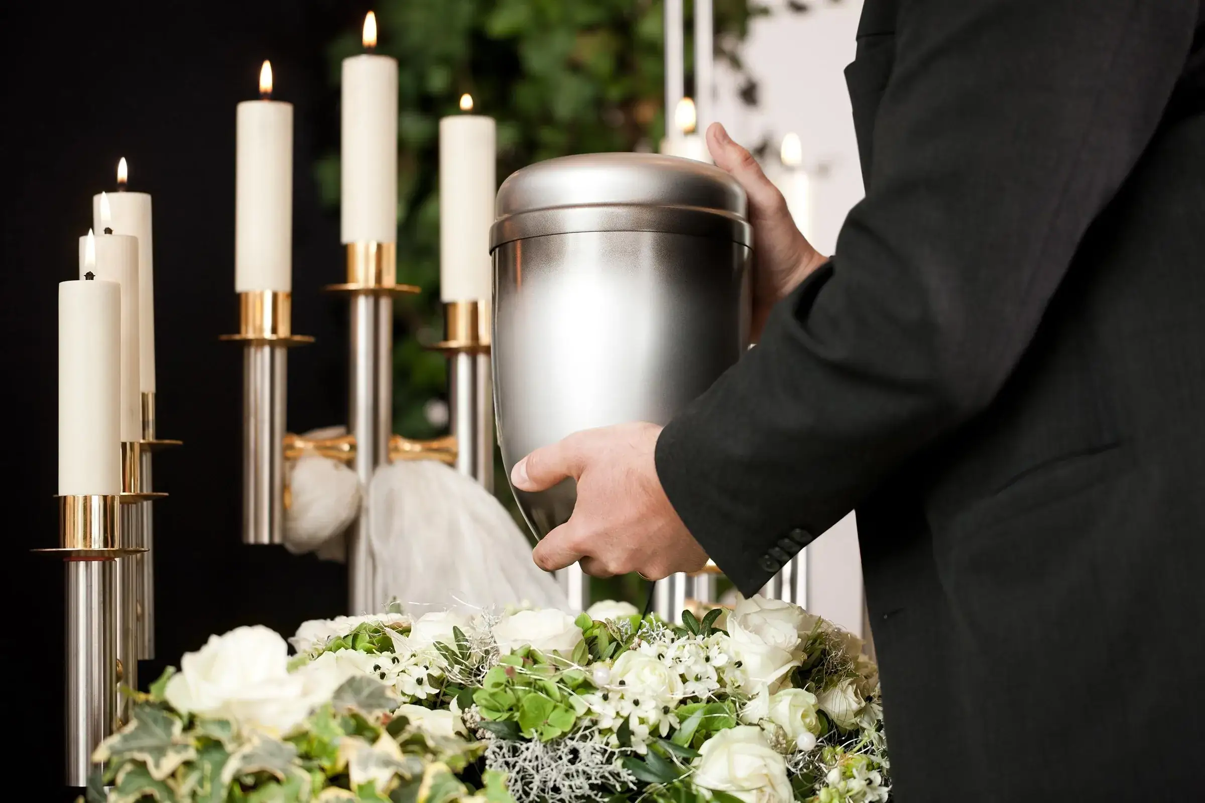 Urnă funerară pentru cenușă, așezată între lumânări și flori albe